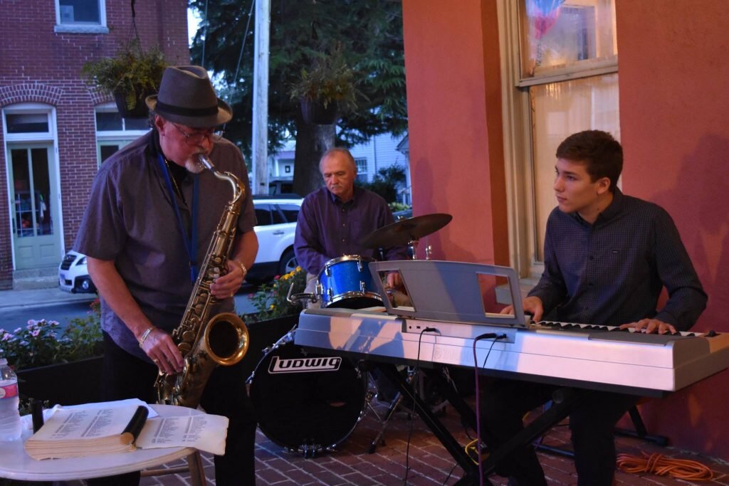 man playing saxaphone with guy on drums and young man on keyboard